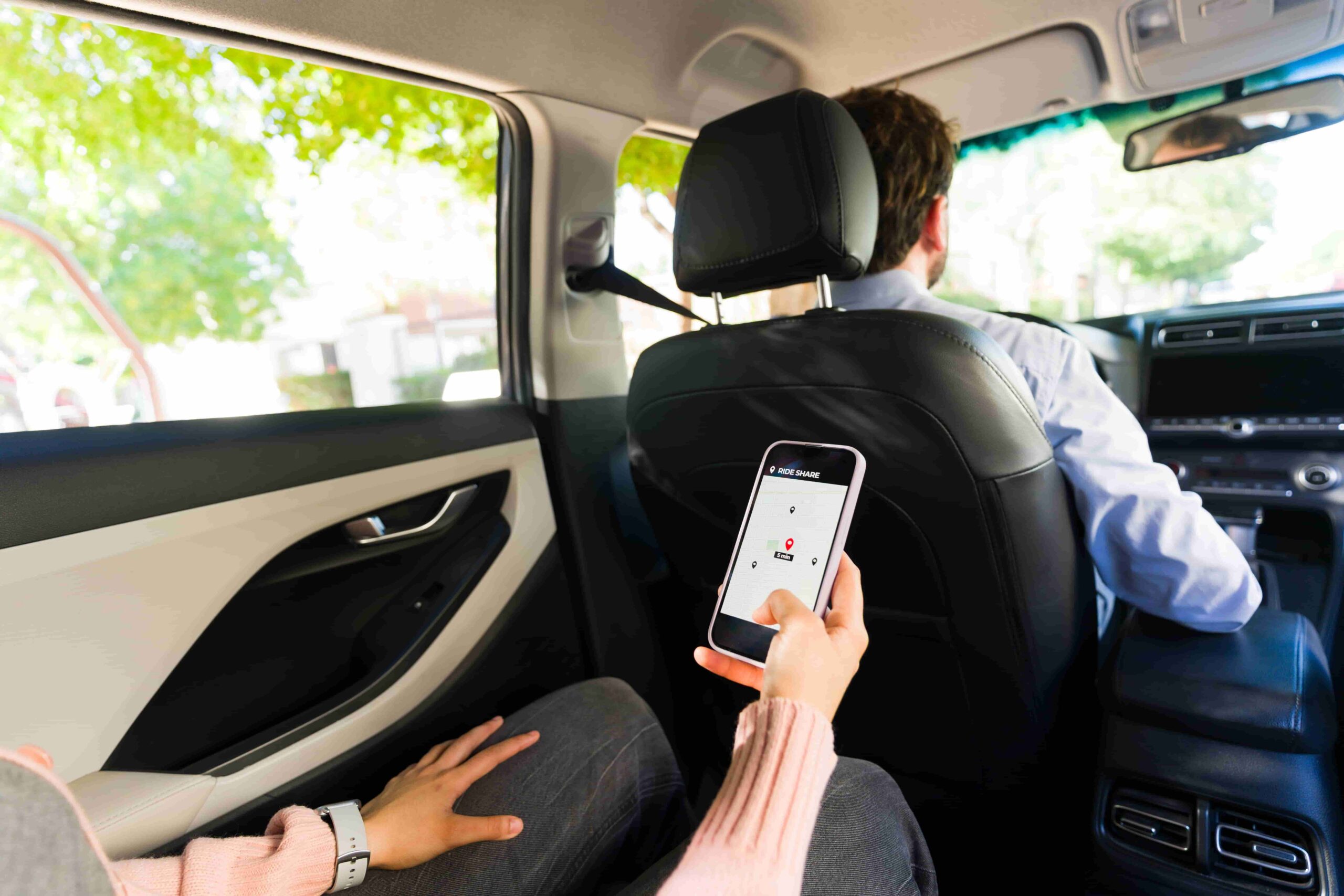Passenger in the back seat of a car using a rideshare app on her phone